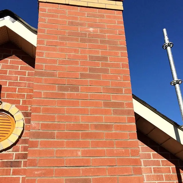 A rebuilt red-brick chimney against a blue sky